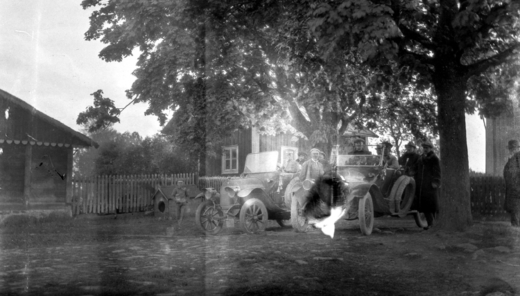 Foto på män vid bilar av märket Dürkopp, tillverkade runt 1912-1914, med bostadshus bakom.

Trol. Tranerås gård i Blekinge. (AB).