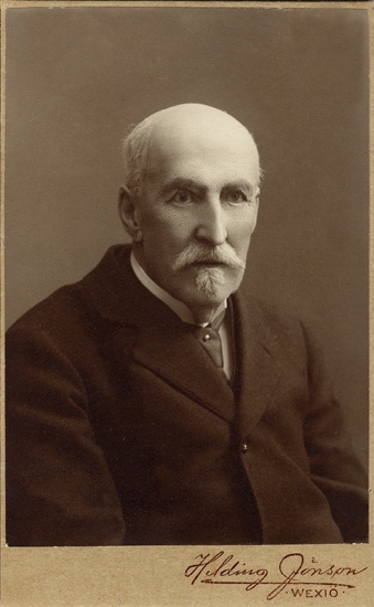 Porträtt (bröstbild, halvprofil) av en äldre man med mustasch och hakskägg.
Han är klädd i mörk kostym och mörk slips med slipsnål.

Friherre August Cederström  (1840-1916), Växjö. Lantbrukare m.m. Ogift.
Son till överste Claes Anton Cederström och h.h. Katarina Fredrika, f. Aschan. 
Källor: Svensk Adelskalender 1904. Gravsten, Tegnérkyrkogården, Växjö.