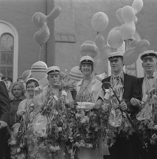 Studenterna, första d. 1960. 
Studenterna har samlats för att lyssna på talet vid Esaias Tegnérs staty. 
I bakgrunden skymtar domkyrkan.