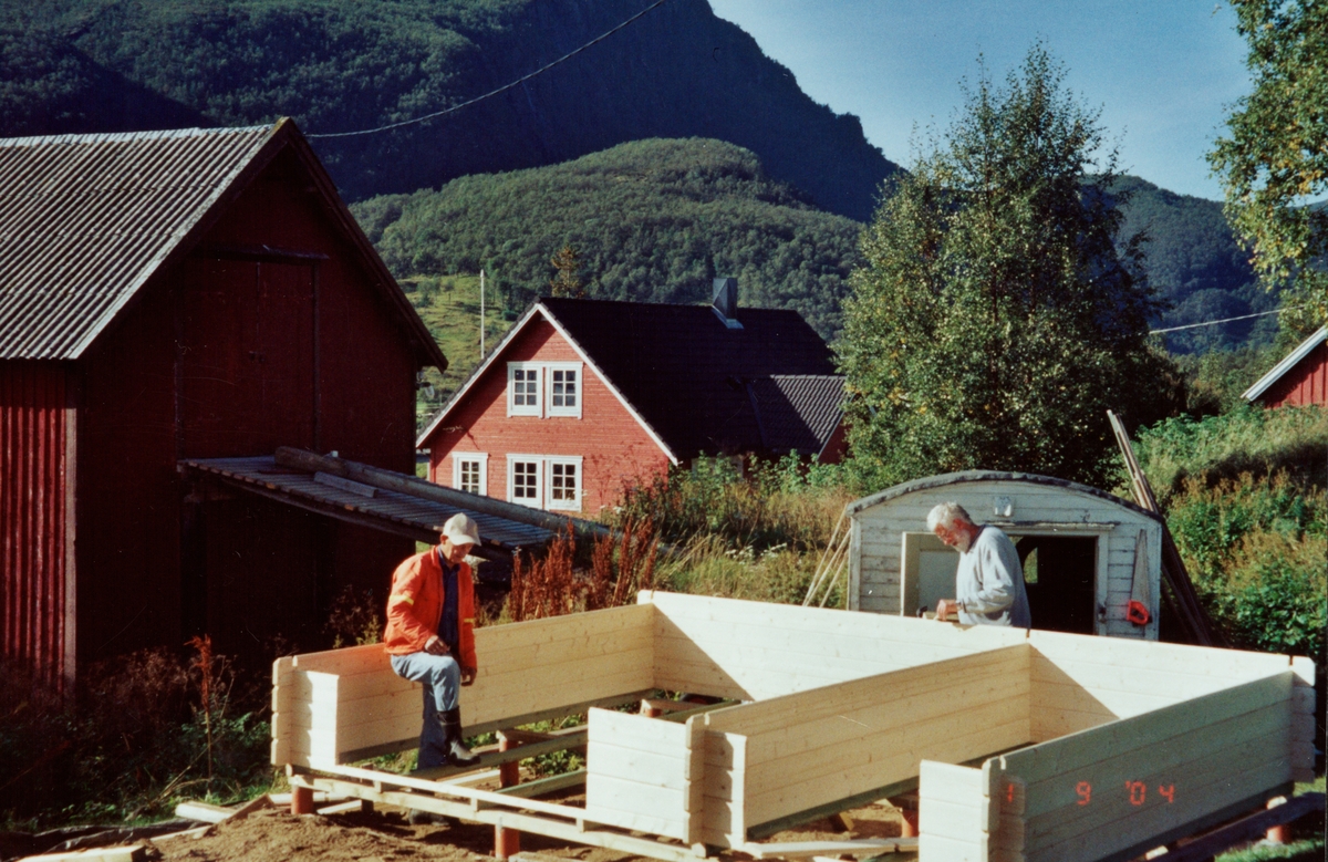 To menn setter opp en bod. Fjøs og låvebru i bakgrunnen.