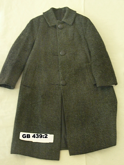 Vinterkappa av svart-grön tweed.
Modell: enkelknäppt med 3 kappar och knapphål. Liten krage, 
stolpfickor, helskuren pingvinärm bak, isydd ärm fram. 
Helfodrad med svart foder.
Inskrivet i huvudkatalogen 1996-1997.
Funktion: Damkappa