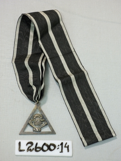 Ett 55 mm brett ripsband(silver-svart-silver-svart-silver) med 
vidhängande dödskalle i en triangel (metall). 
Frimurarorden.

Inskrivet i huvudboken 1933
Funktion: Ordenstecken inom Frimurarorden