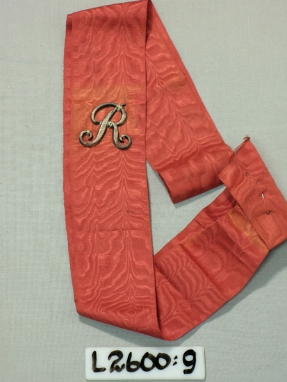 Ett 60 mm brett rött ripsband med ett påsytt "R" i vitmetall.

Inskrivet i huvudboken 1933
Funktion: Ordenstecken