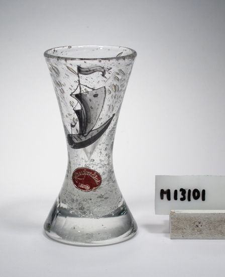 Brännvinsglas. Tillhör servis "Platon".
Glaset blåsigt (posten doppad i alspån).
Målat i grått ett skepp.
Ofärgat, tämligen klart glas.
Höjd 106 mm, övre diameter 53 mm, undre diameter 56 mm.
Inskriven i huvudkatalgen 1943.

Se även M 13102 och M 13108, samma modell.
Funktion: Brännvinsglas