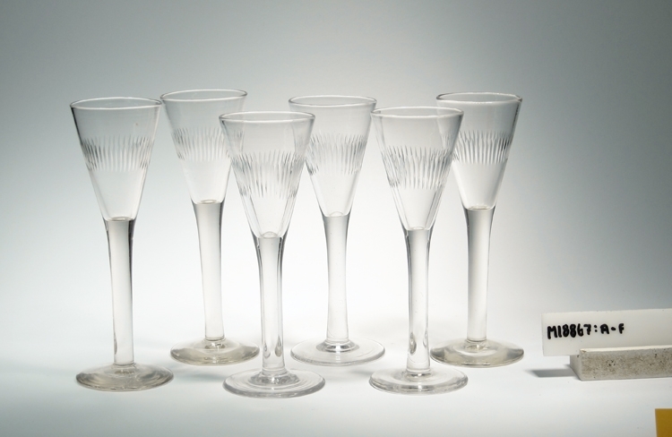 Spetsglas tillhörande servisen "Juno", vilken först tillverkades vid Kosta glasbruk med början år 1892, senare även tillverkad vid Reijmyre och Limmared m.fl. glasbruk.
Konisk kupa, cylindriskt ben och skivfot. Täta lodräta räfflor runt mitten av kupans utsida.
Ofärgat klarglas.
Ovan angivna mått avser övre diameter och kupdjup.
Bendiameter: 10 mm, fotdiameter: 52 mm, fothöjd: 7,5 mm, och väggtjocklek: 2 mm.
Inskrivet i huvudkatalogen 1966.
Funktion: Brännvinsglas