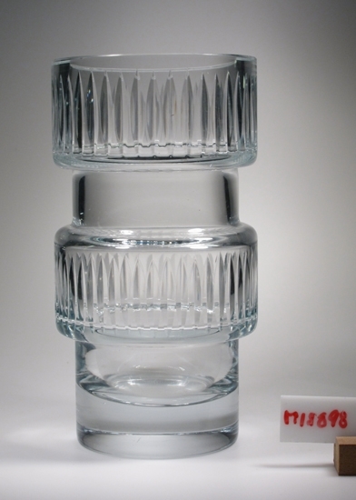 Vas.
Cylindrisk, med två raka utbuktningar som är slipade 
med lodräta slipade skär.
Klarglas.
Funktion: Blomvas