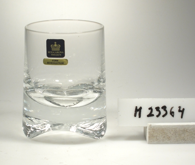 Tumlare. Tillverkat av Krona Bruken, Åseda glasbruk.
Formgivare: Bo Borgström.
Beskrivning: Konad (smalnar upptill). Tjock botten med tre uddar.
Färg: Ofärgat klarglas.
Kristallglas?
Mått: Ovan angivna mått avser övre diameter.
Bottendiameter: 70 mm.
Fyrkantig, svart etikett med en krona och guldtext: Se "Signering, märkning" 1 ovan.
Avlång guldetikett med text: Se "Signering, märkning" 2 ovan.
Inskrivet i huvudkatalogen 1975.

Ur "Glas 75" utställningsglas.
Funktion: Tumlare