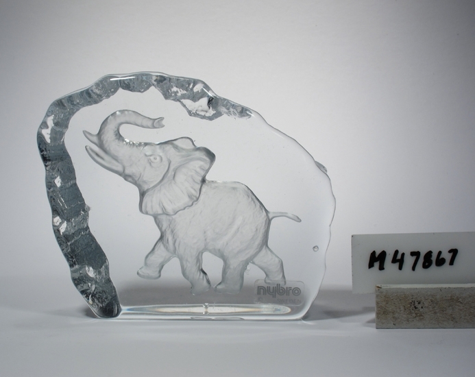 Glasblock med elefant.
Konstnär: Rune Strand.
Troligen tillverkat under 1990-talet.
Beskrivning: Flat glasskiva med oregelbunden kant. Motiv i form av en trumpetande elefant.
Färg: Ofärgat klarglas.
Teknik: Stöpt och blästrat.
Inskrivet i huvudkatalogen tidigast 1995.
Funktion: Glasblock, prydnadsföremål.