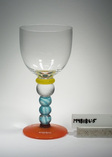 Vitvinsglas "Fenix".
Art.nr. 25305.
Konstnär: Kjell Engman.
Beskrivning: Tulpanformad kupa, mellanring, bats, räfflat ben.
Färg: Kupa av ofärgat klarglas, gul ring, turkosrandigt ben, orange fot.
Mått: Ovan angivna diameter avser övre diameter. Fotdiameter: 70 mm.
Stämplad märkning samt klar etikett med vit text Se "Signering, märkning" ovan.
Inskrivet i huvudkatalogen tidigast 1996.
Funktion: Vitvinsglas