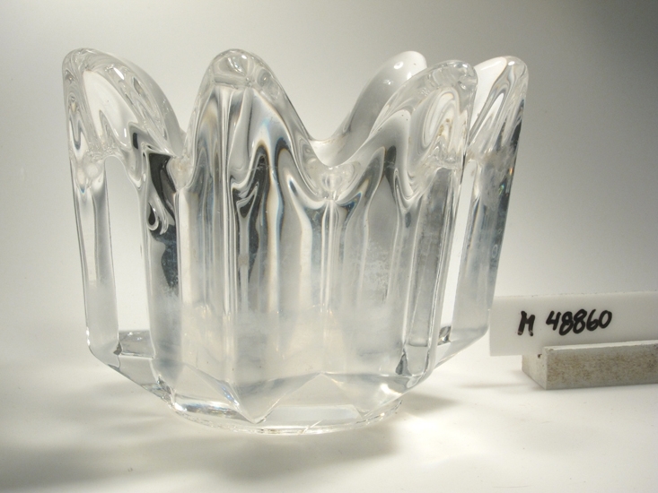 Glasskål.
Rund, ganska smal form, glaset är format som en blomma,
med hål i mitten.
Klarglas.
Funktion: Skål