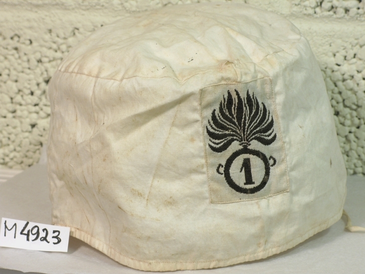 Solskydd till uniformsmössa. 
Vit trol. bomullslärft ev. lin.
Framtill i svart och vitt, facklan och nr 1. I nedkant sydd dragsko, med iträtt band.
Tillhör italiensk uniform, se M 4915.

Inskrivet i huvudbok 1930.
Funktion: Att skydda huvudbonaden mot starkt solljus.