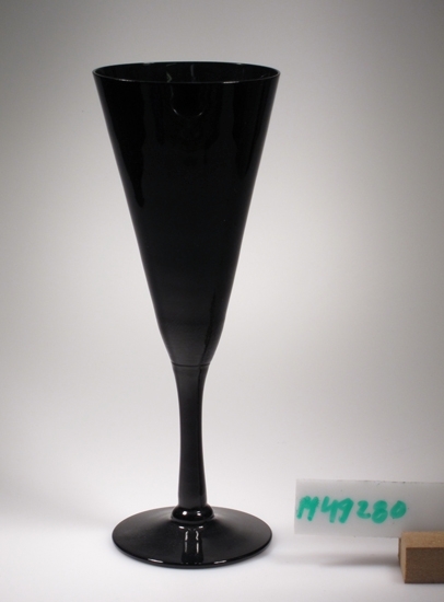 Champagneglas.
Beskrivning: Trumpetformad kupa. Påsatt, draget ben. 
Skivfot. Sprängt.
Färg: Svart klarglas.
Mått: Diameter ovan avser fotdiametern.
Inskrivet i huvudkatalogen 2005.
Funktion: Champagneglas