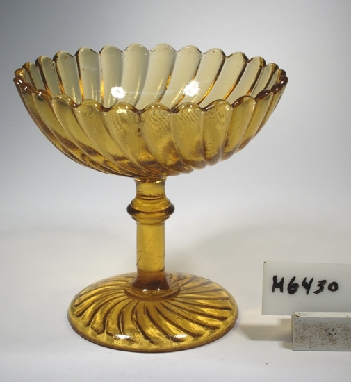 Sockerskål.
Beskrivning: "Turbin" på ben och fot. Svängda räfflor. Ben med knapp.
Färg: Brungult, halvopakt glas.
Mått: Ovan anges övre diameter. Fotdiameter: 79 mm.
Inskrivet i huvudkatalogen 1934.
Funktion: Sockerskål