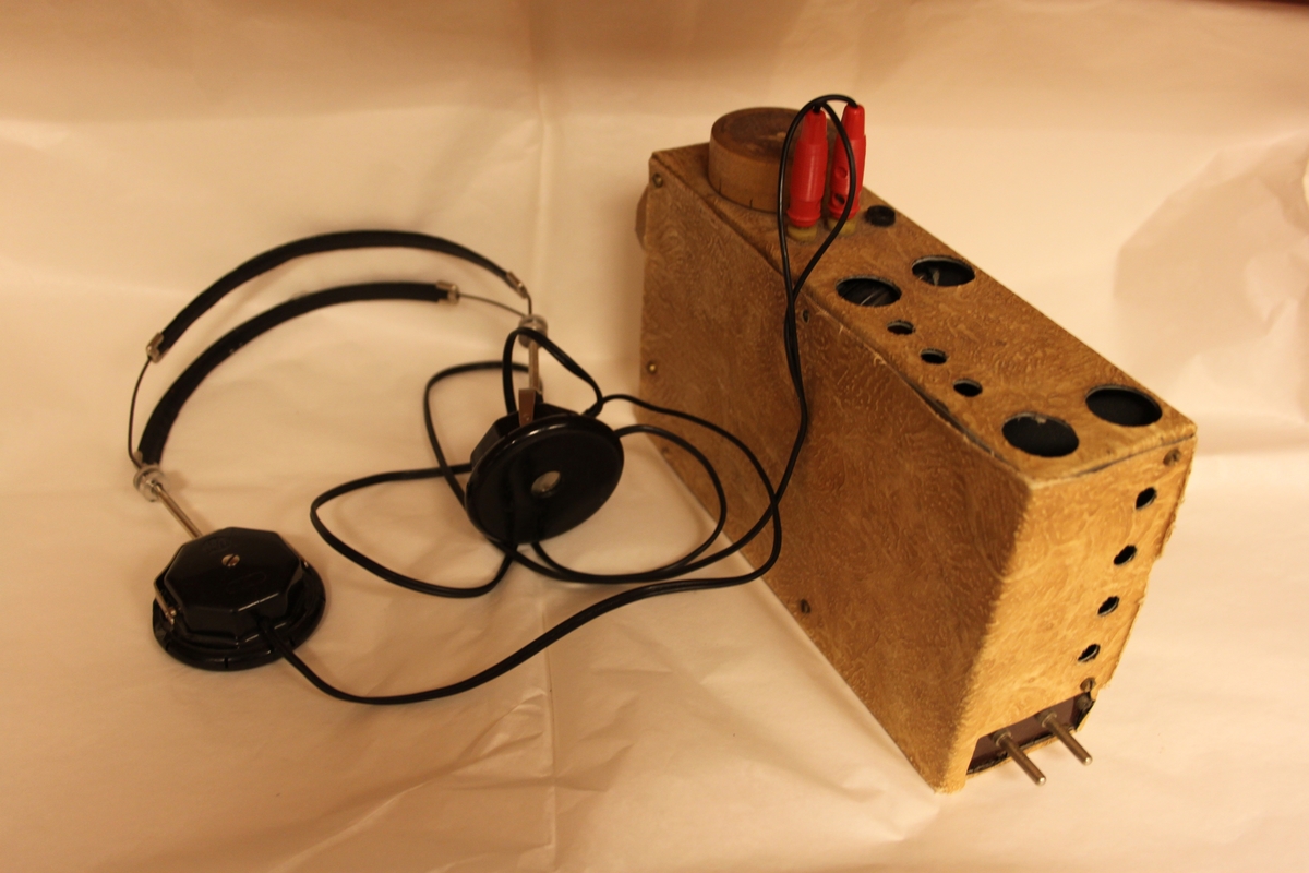 Radiomottaker, hjemmelaget. Rektangulært chassi laget i trefiner.. Med sorte høretelefoner med stempel OMEGA. Dette eksemplaret er fortsatt i utmerket stand. Det følger også med en improvisert antenne.