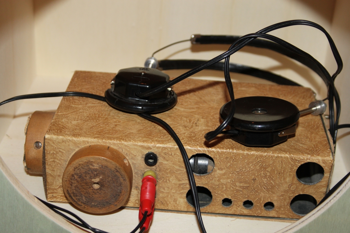 Radiomottaker, hjemmelaget. Rektangulært chassi laget i trefiner.. Med sorte høretelefoner med stempel OMEGA. Dette eksemplaret er fortsatt i utmerket stand. Det følger også med en improvisert antenne.