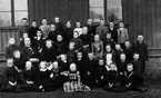 Andra klassen av Falköpings folkskola vårterminen 1900 utanför norra gavelväggen. 1: Sahlkvist, Oskar, Agnestad 2: Nyberg, Karl, Hästhagen 3: Johansson, Gunnar, Blåsås 4: Frid, Tekla, Falköping 5: Hofman, Klara, Gunnestorp 6: Gustavs, Anna, (stenk), Mossen 7: Andersson, Ruth, Falköping 8: Båth, Sven, Prästgatan 9: Hellström, Gustav, 10: Haglund, Olof, 11: Bengtsson, Gestrud, (Gertrud) ? 12: Svensson, Ivan, Gasvägen, 13: Hedbom, Emil, Forsens 14: Eriksson, Hildur, Banv, Sköttning 15: Jofur, Emma, 16: Gustafsson, Hanna, 17: Olsson, Anna, 18: Holm, Arvid, Banv, Sköttning 19: Sederholm, Karl, Annedal 20: Linnmann, Oskar, 21: Lärare Fast, J.A. 22: Holm, Anna Öfr. Gärdesgatan 23: Sand, Märtha, Storgatan 24: Syrén, Hilma, Bestorp 25: Karlsson, Anna, Öfr. Gärdesgatan 26: Hasselberg, Yngve, Sikagården 27: Larsson, Ferdinand, Öfr Gärdesgatan 28: Melin, Oskar, Nygatan 29: Andersson, Edit, Ledsgården, Bestorp 30: Vickström, Judith, Kyrkogatan 31: Olsson, Alma, Nygatan 32: Krall, Beda,