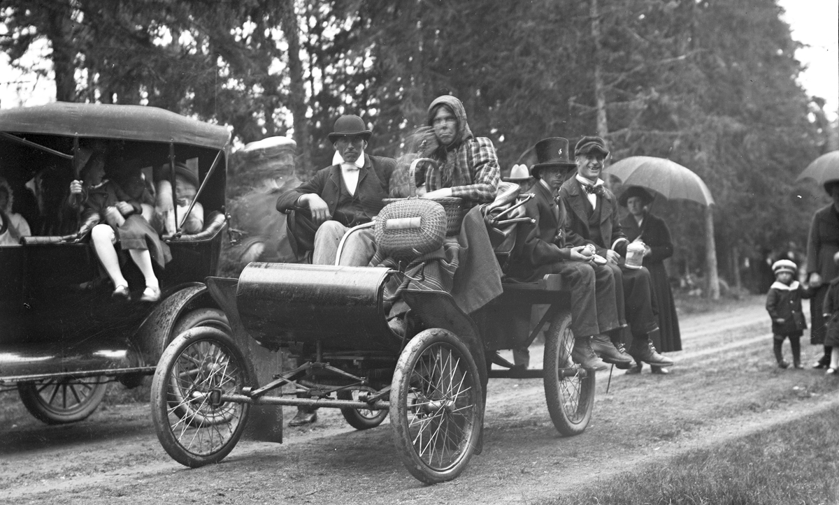 Barnens dag i Storvik 1921. Bilen är en 1903 Oldsmobil. Ägare Helmer Widlund Storvik. Samma man som på mitten av 1930-talet byggde en av dom första TV-apparaterna i Sverige. Bilden tagen vid Barnens Dag i Storvik början på 1920-talet. Mannen med korgen i framsätet heter Gustav Berlin, Storvik, och bakerst på bilen sitter "glas"-Hjalmar Persson, Bro Storvik.