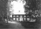 Berggården, fotografens hem i Östansjö. Personerna som sitter framför bron är från vänster Ester Lindberg med dottern Majly, Elvira Lindberg med sonen Folke samt Per H Lindberg. Ester, Elvira och Per är barn till Per Lindberg.