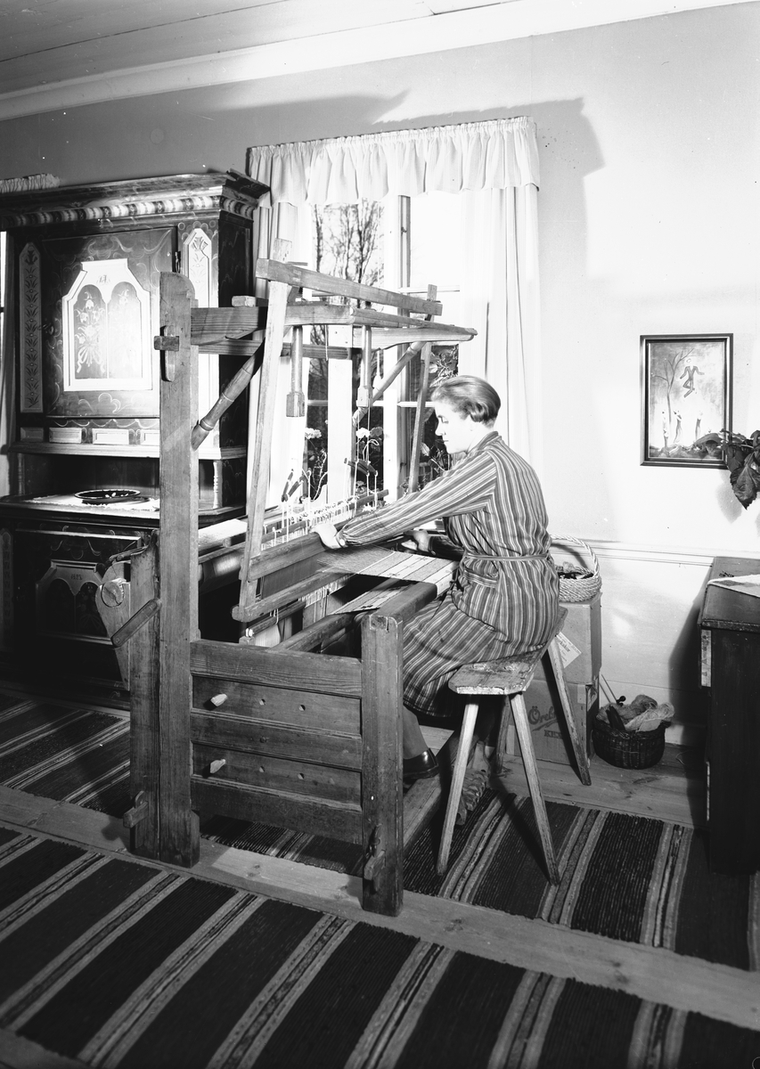 Från boken "Svenska Hem i ord och bilder" från 1944. Hemma hos Konstnären Manne och Brita Östlund, ägare till Jons i Västbyggeby. Fru Brita Östlund vid vävstolen. Till vänster ett mörkblått Järvsöskåp med röda speglar från 1825.