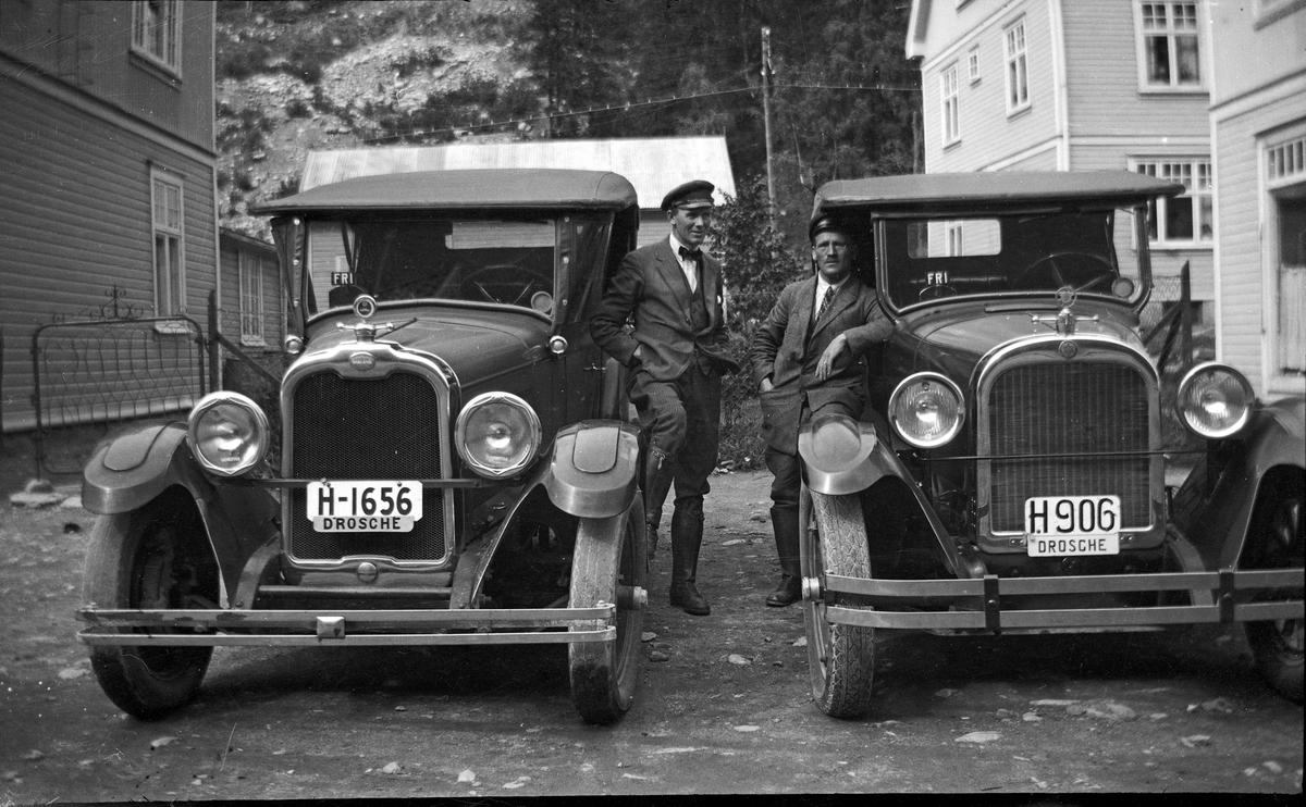 To drosjebiler med sjåfører stående på utsiden. Bilene står parkert ved Brødrene Foss kolonial på Ingolfsland.