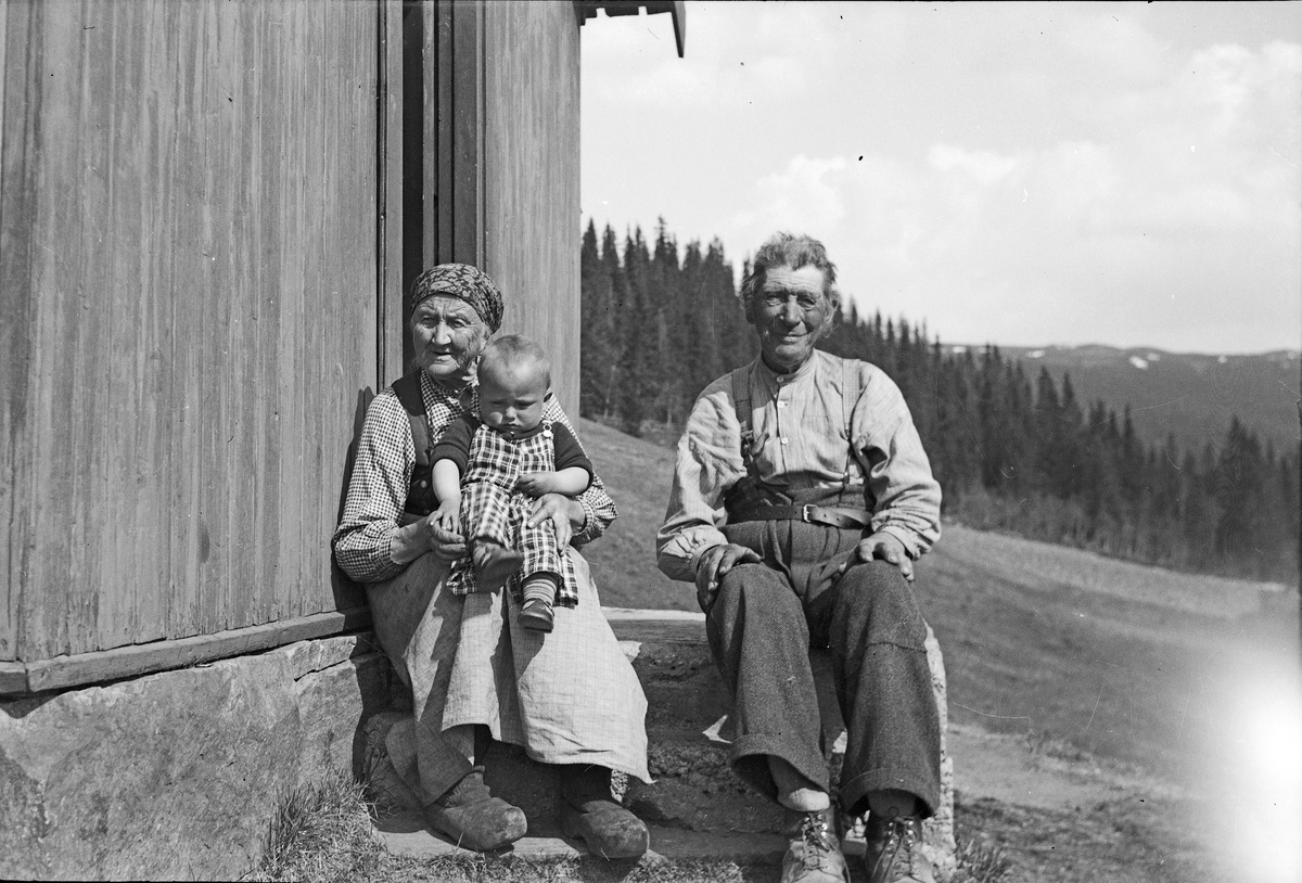 Eldre ektepar sittende på steintrapp. Kvinnen har en liten gutt, Bjørn Holtan, på fanget.