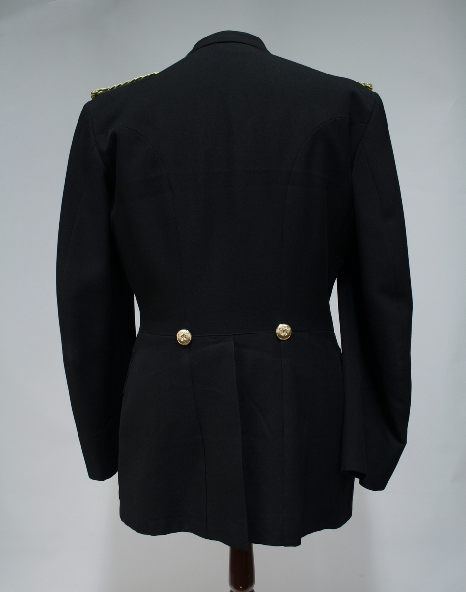 Uniform for politinspektør etter 1963-reglement med merking etter 1977-reglement. Helårsuniform M/1963 med skjorte, langbukse, belte, helårskappe og jakke. Skyggelue med gullbrodert bånd, loslue og båtlue M/1967. Kappen og jakken har skulderklaffer av flettede gullsnorer med to sølvstjerner og festeknapp i gullbroderi. Skjorten har en enklere skulderklaff med to gule render og to sølvstjerner. Det følger med et ekstra enkelt lærbelte og et ekstra sett skulderklaffer til skjorte. Plaggene har gullfargede løveknapper.