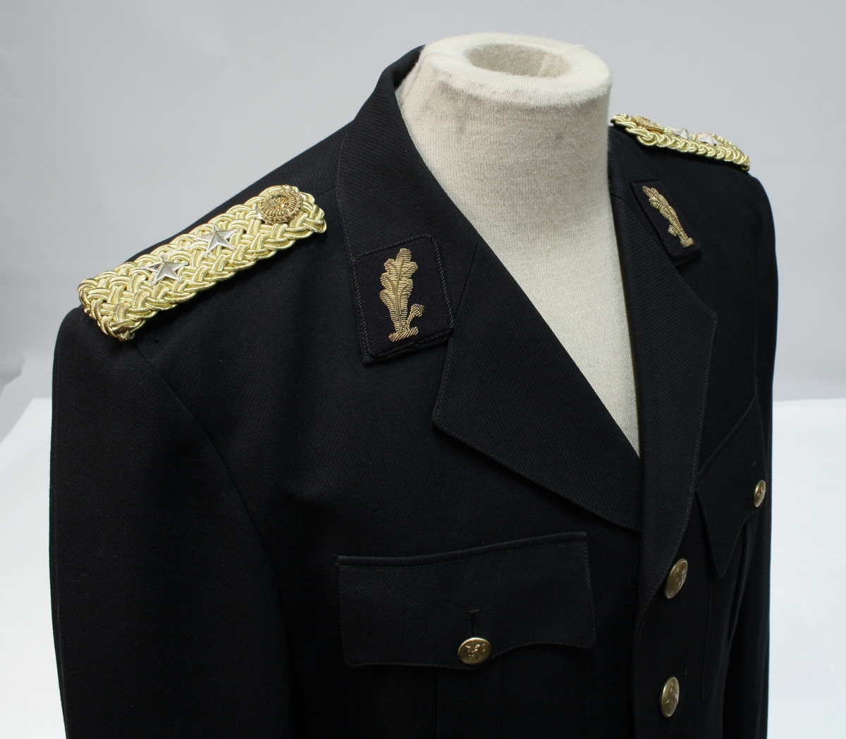 Uniform for politinspektør etter 1963-reglement med merking etter 1977-reglement. Helårsuniform M/1963 med skjorte, langbukse, belte, helårskappe og jakke. Skyggelue med gullbrodert bånd, loslue og båtlue M/1967. Kappen og jakken har skulderklaffer av flettede gullsnorer med to sølvstjerner og festeknapp i gullbroderi. Skjorten har en enklere skulderklaff med to gule render og to sølvstjerner. Det følger med et ekstra enkelt lærbelte og et ekstra sett skulderklaffer til skjorte. Plaggene har gullfargede løveknapper.