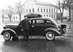 Chaufför P J Green vid en X307 förlängd 1937  Dodge D-5 Touring Sedan med gengasaggregat på Teaterplan vid Staketgatan i Gävle. I bakgrunden Norra Rådmansgatan 20. I bakgrunden Sjöströms mekaniska verkstad.