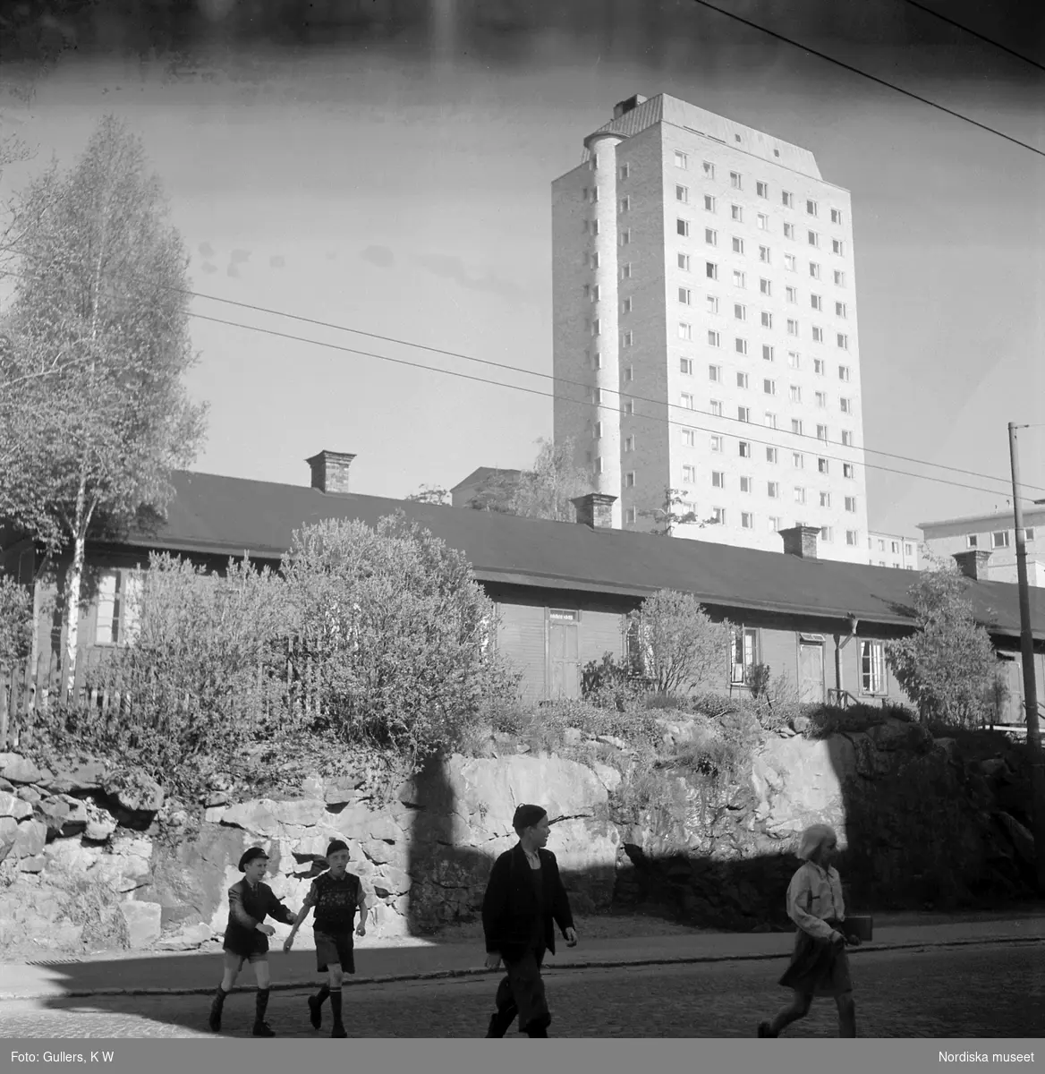 Mariebergsgatan, Kungsholmen, Stockholm. I bakgrunden det s k Kvinnohuset på Welanders väg 12 med äldre baracker nedanför. I förgrunden en grupp barn som går över gatan.