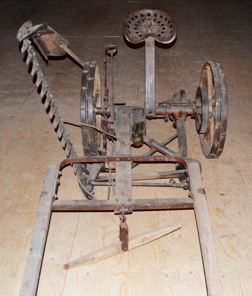 Slåmaskin for hest med drag. 6-eika metallhjul. Sete. Jarn, utan draget, som er i tre.