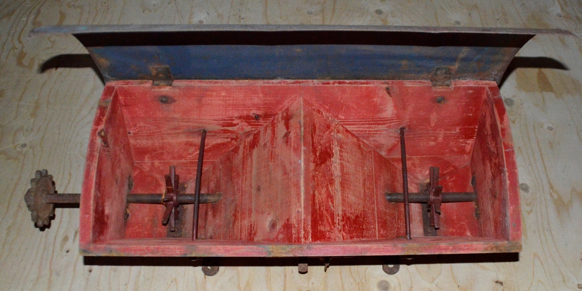 Truleg topp til såmaskin. Trekasse med metall lok. Oppi kassa eit lite hol i kvar ende. Treet er farga raudt.
