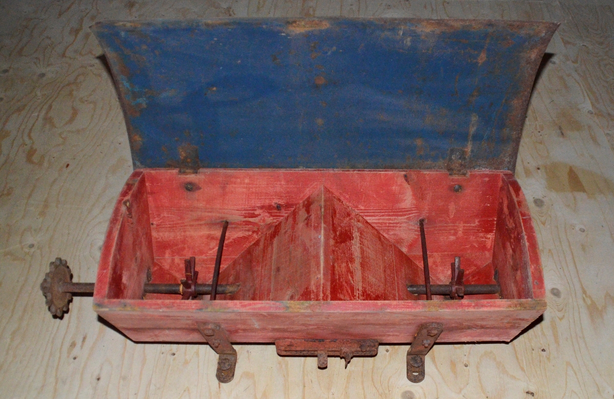 Truleg topp til såmaskin. Trekasse med metall lok. Oppi kassa eit lite hol i kvar ende. Treet er farga raudt.