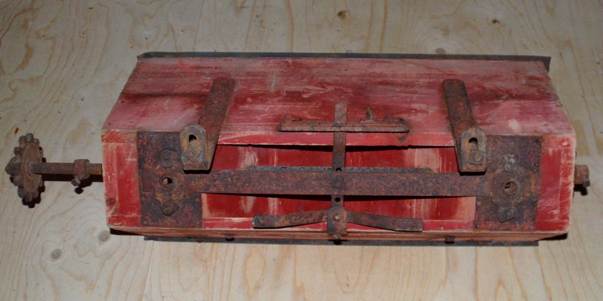 Truleg topp til såmaskin. Trekasse med metall lok. Oppi kassa eit lite hol i kvar ende. Treet er farga raudt.