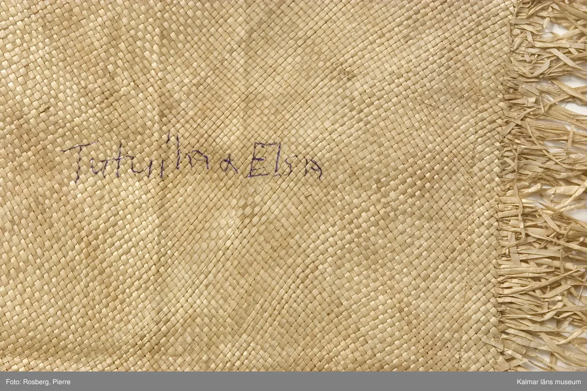 KLM 28465. Matta/kjol av pandanus (en palmväxt) och fjädrar. Plagget benämns 'ie toga. 'ie är en av tre sorters odlade palmväxter som används av samoanerna för mattorna. Mattan är mer att betrakta som ett ceremoniellt klädesplagg flätat av pandanus med fransar i båda ändarna och dekorerat med röda och några få vita fjädrar fastsydda med maskinsöm. Den här mattan, är ett ceremoniellt klädesplagg, den bärs runt midjan som en kjol, dubbelvikt så att man skall kunna se fransarna. Den hålls vanligen på plats av en gördel av barktyg. Följande namn finns påskrivna, på framsidan, KELEmet, TutuilA x Elsa, LUIT; på baksidan, AiLUA Poliko, LEALA SOLA. Därutöver ett nummer som tycks vara 10 finns också. Tutuila är för övrigt namnet på en sydöstsamoansk ö, vilken är huvudön i Amerikanska Samoa.