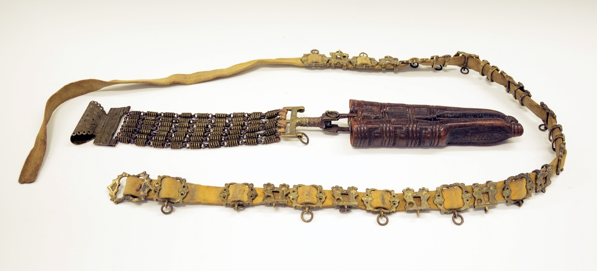 Fra protokollen: Tvislir med 1 kniv og belte av semska skinn med smøygjestolar av massing med ein nedhangande ring or kvar stol eller kvar sylgje. Beltekroken er bladforma, uthoggin (gravert) i strikmynster, fraa denne gjeng 7 taattar traadlekkje, av massing og forma som kyrmaal-taattar. Kniven med treskaft (barlind) og svære, støypte i massing - holkar (uthogne) støypte i rank eller strik. I enden paa bakholken kvardar rundt og krosslykkje i tverenden. Knivsbladet langt, med sneideslipa odd-fase i bakken. Slirine med fergd strik-ornamentik. Paa den eine innskrifti K.A.S.H, paa den andre: ANNO 1731.
Fra Telemarki eller Sæterdalen.
