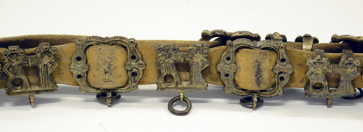 Fra protokollen: Tvislir med 1 kniv og belte av semska skinn med smøygjestolar av massing med ein nedhangande ring or kvar stol eller kvar sylgje. Beltekroken er bladforma, uthoggin (gravert) i strikmynster, fraa denne gjeng 7 taattar traadlekkje, av massing og forma som kyrmaal-taattar. Kniven med treskaft (barlind) og svære, støypte i massing - holkar (uthogne) støypte i rank eller strik. I enden paa bakholken kvardar rundt og krosslykkje i tverenden. Knivsbladet langt, med sneideslipa odd-fase i bakken. Slirine med fergd strik-ornamentik. Paa den eine innskrifti K.A.S.H, paa den andre: ANNO 1731.
Fra Telemarki eller Sæterdalen.
