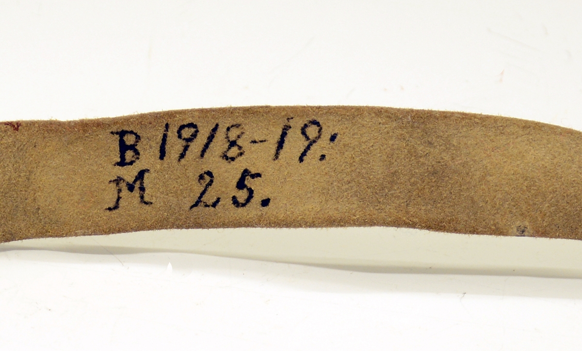 Fra protokollen: Tvislir med 1 kniv og belte av semska skinn med smøygjestolar av massing med ein nedhangande ring or kvar stol eller kvar sylgje. Beltekroken er bladforma, uthoggin (gravert) i strikmynster, fraa denne gjeng 7 taattar traadlekkje, av massing og forma som kyrmaal-taattar. Kniven med treskaft (barlind) og svære, støypte i massing - holkar (uthogne) støypte i rank eller strik. I enden paa bakholken kvardar rundt og krosslykkje i tverenden. Knivsbladet langt, med sneideslipa odd-fase i bakken. Slirine med fergd strik-ornamentik. Paa den eine innskrifti K.A.S.H, paa den andre: ANNO 1731.
Fra Telemarki eller Sæterdalen.