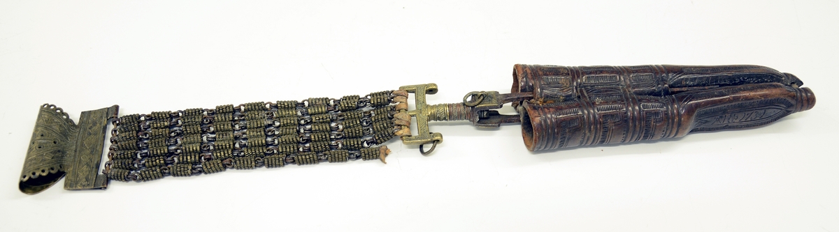 Fra protokollen: Tvislir med 1 kniv og belte av semska skinn med smøygjestolar av massing med ein nedhangande ring or kvar stol eller kvar sylgje. Beltekroken er bladforma, uthoggin (gravert) i strikmynster, fraa denne gjeng 7 taattar traadlekkje, av massing og forma som kyrmaal-taattar. Kniven med treskaft (barlind) og svære, støypte i massing - holkar (uthogne) støypte i rank eller strik. I enden paa bakholken kvardar rundt og krosslykkje i tverenden. Knivsbladet langt, med sneideslipa odd-fase i bakken. Slirine med fergd strik-ornamentik. Paa den eine innskrifti K.A.S.H, paa den andre: ANNO 1731.
Fra Telemarki eller Sæterdalen.