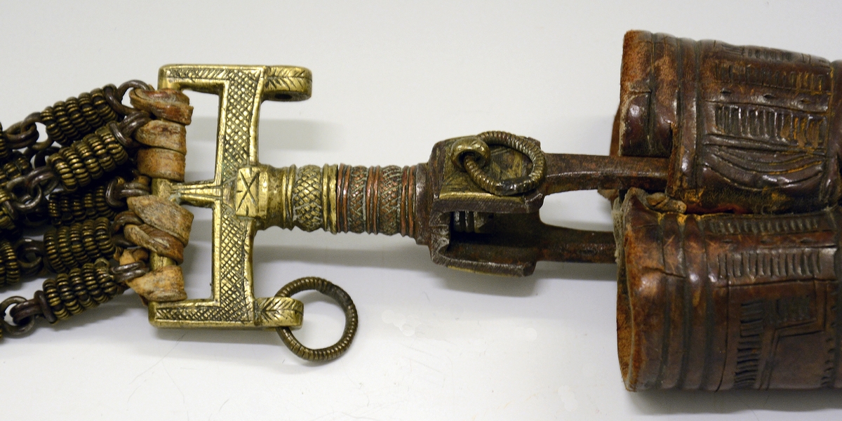 Fra protokollen: Tvislir med 1 kniv og belte av semska skinn med smøygjestolar av massing med ein nedhangande ring or kvar stol eller kvar sylgje. Beltekroken er bladforma, uthoggin (gravert) i strikmynster, fraa denne gjeng 7 taattar traadlekkje, av massing og forma som kyrmaal-taattar. Kniven med treskaft (barlind) og svære, støypte i massing - holkar (uthogne) støypte i rank eller strik. I enden paa bakholken kvardar rundt og krosslykkje i tverenden. Knivsbladet langt, med sneideslipa odd-fase i bakken. Slirine med fergd strik-ornamentik. Paa den eine innskrifti K.A.S.H, paa den andre: ANNO 1731.
Fra Telemarki eller Sæterdalen.