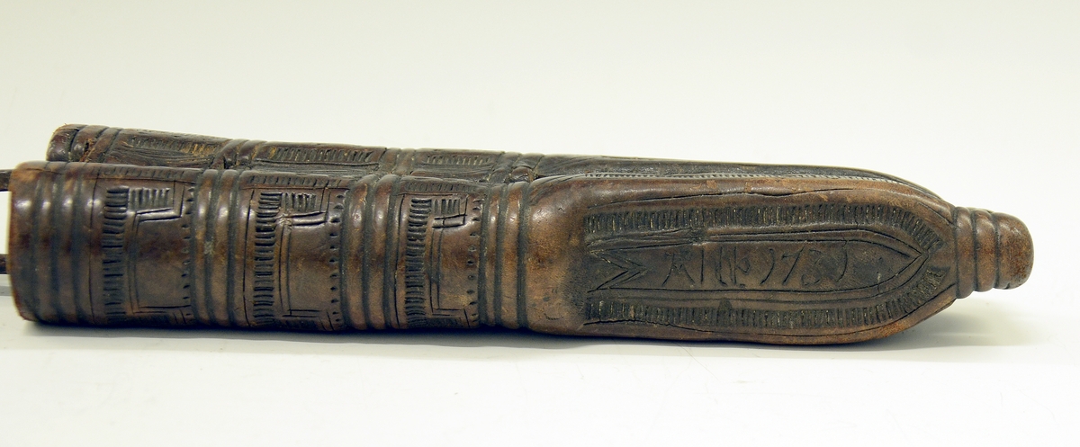 Fra protokollen: Tvislir med 1 kniv og belte av semska skinn med smøygjestolar av massing med ein nedhangande ring or kvar stol eller kvar sylgje. Beltekroken er bladforma, uthoggin (gravert) i strikmynster, fraa denne gjeng 7 taattar traadlekkje, av massing og forma som kyrmaal-taattar. Kniven med treskaft (barlind) og svære, støypte i massing - holkar (uthogne) støypte i rank eller strik. I enden paa bakholken kvardar rundt og krosslykkje i tverenden. Knivsbladet langt, med sneideslipa odd-fase i bakken. Slirine med fergd strik-ornamentik. Paa den eine innskrifti K.A.S.H, paa den andre: ANNO 1731.
Fra Telemarki eller Sæterdalen.