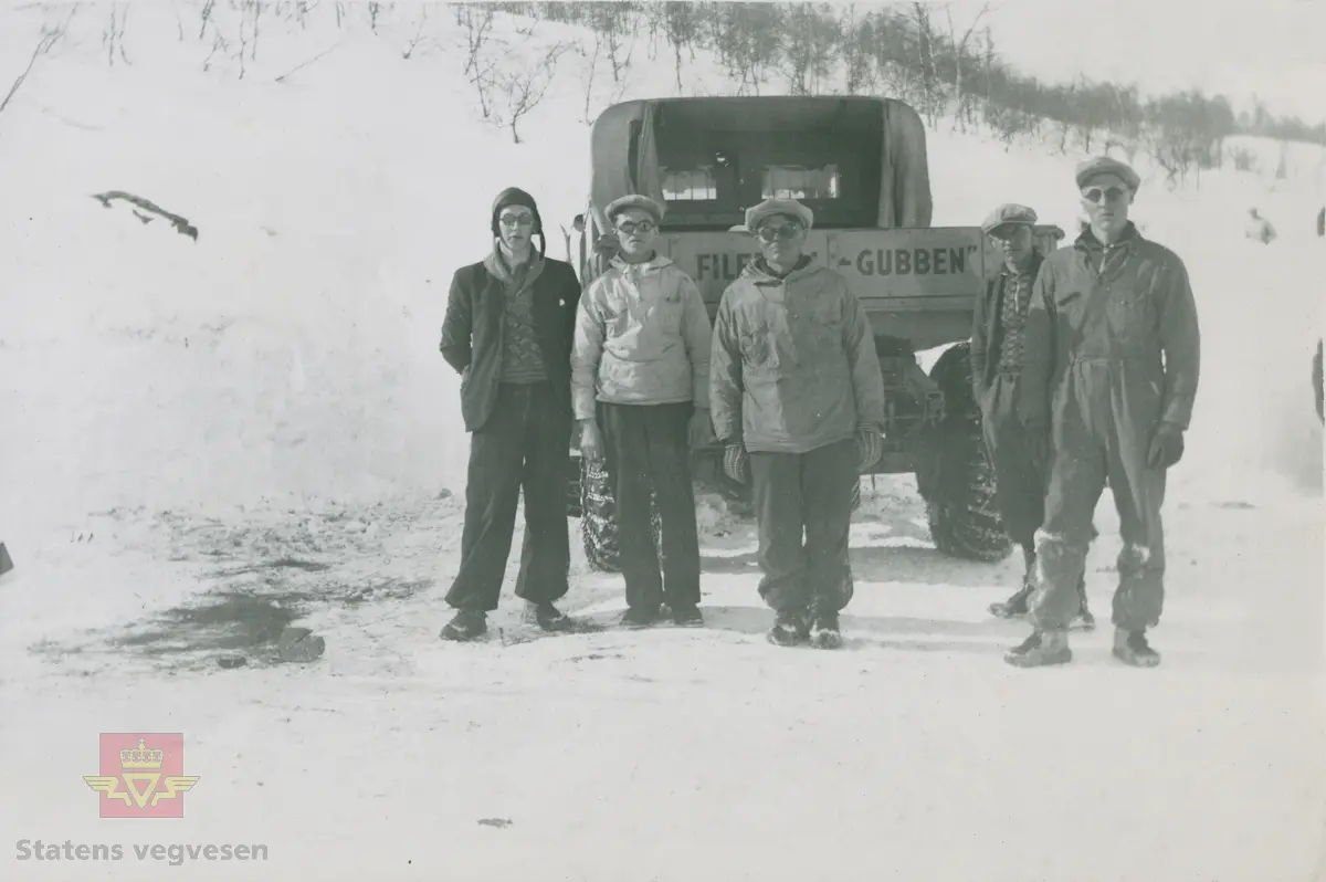 Tekst på bildet "Filefjell-Gubben". FWD lastebil modell SU fra A/S Jotunheimen og Valdresruten Bilselskap (JVB) med kjennetegn E-3928. Bilen ble levert til Jotunheimen, Valdresruten i 1936, og holdt vegen over Filefjell åpen. Klikk på pilen til høyre for å se tilleggsbilder: Legg merke til benkene på lasteplanet med tak og presenning til ly for vær og vind for brøytemannskap.   
Etter en tøff vinter 1936-1937 mottok Colbjørnsen brev fra JVB, A/S Jotunheimen og Valdresruten Bilselskap  30.04.1937, hvor de sier seg meget fornøyd med bilen de kjøpte før jul i 1936. Jf. boka "Familiefirmaet-utenom allfarvei/2000 Årsboken."Colbjørnsen & Co A/S, av Bjørn Ausjen Johannessen. Bilde av "Filefjell-Gubben" i A/S Jotunheimen og Valdresruten Bilselskap  på en av veivesenets garasjer på Filefjell vises i tilleggbildene.  FWD lastebilen "Filefjell-Gubben" ble innkjøpt av JVB  i 1936. Den til da kraftigste i landet. Vegfolk kom da også fra fjern og nær for å bivåne brøytingen, og for å se og lære. 
 "A/S Jotunheimen og Valdresruten Bilselskap  ble etablert i 1919 og har vært selve livsnerven gjennom Valdresbygdene. "Filefjell-Gubben" ble satt inn i arbeidet med å holde Filefjellvegen oppe. Med felles innsats og arbeid fra Staten og selskapets side, lykkes det å holde Filefjellvegen farbar for vintertrafikk vinteren 1936-1937, den første fjellovergang i Norge som var åpen året rundt." Jf. Kilde: "JVB. Den spede begynnelse-A/S Jotunheimen og Valdresruten Bilselskap."  
Personene på bildet er ukjente. Bildene som vises er både fra Oslo og Filefjell. 
Bildene er registrert enkeltvis på nr: 
Bilde 2) NVM 00-F-33671
Bilde 3  NVM 00-F-33672
Bilde 4  NVM 00-F-33704
Bilde 5) NVM 00-F-33705
Bilde 6) NVM 00-F-33707
Bilde 7) NVM 00-F-33708
Bilde 8) NVM 00-F-33710
Bilde 9) NVM 00-F-33711
Bilde 10)NVM 00-F33659
Bilde 11)NVM 00-F33660