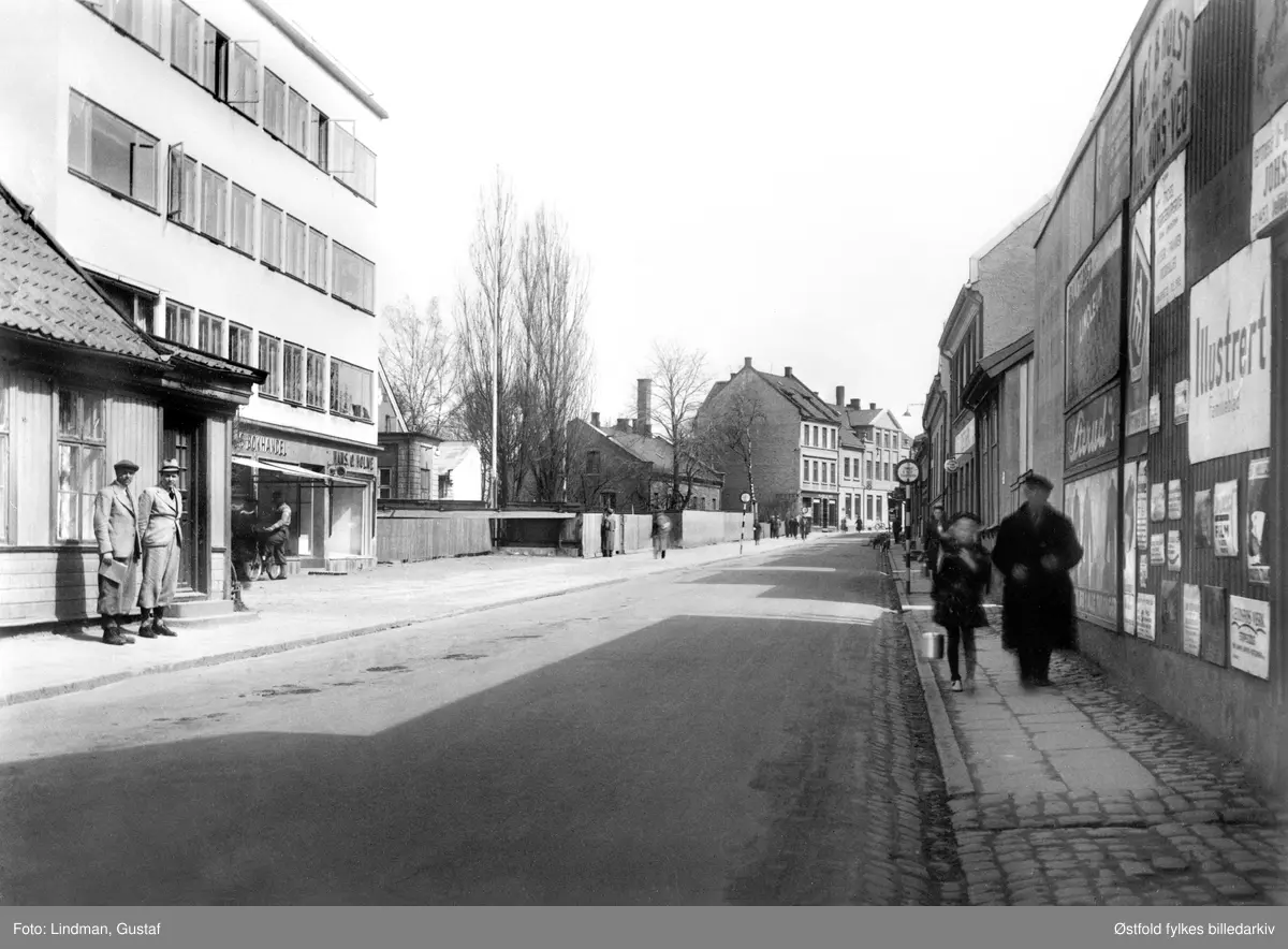 Gateparti fra Storgata i Moss 1941. Til venstre en bokhandel. Fortauet til høyre har brostein. Helt til venstre står ingeniør Johan Hoel og formannskapssekretær Arne Kinander ved Storgata 2. Flotte eplenikkers!