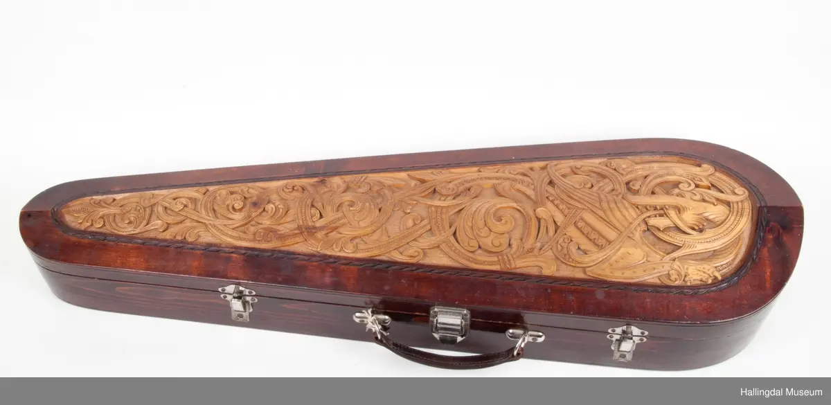 Lokket er utskjært med drake og båndslynginger.  Utskjæringer inne i felekassen.  5 rom med lokk i kassen.  3 lokk har utskjæringer med motiver fra hallingdans.  
Skaftet er besatt med perlemor, rosetegning i sort, dyrehode øverst på skaftet.  4 strenger over og 4 strenger under strengbrettet.  2 felebuer rødbrun mahogni.  Fela se HFN 03210.