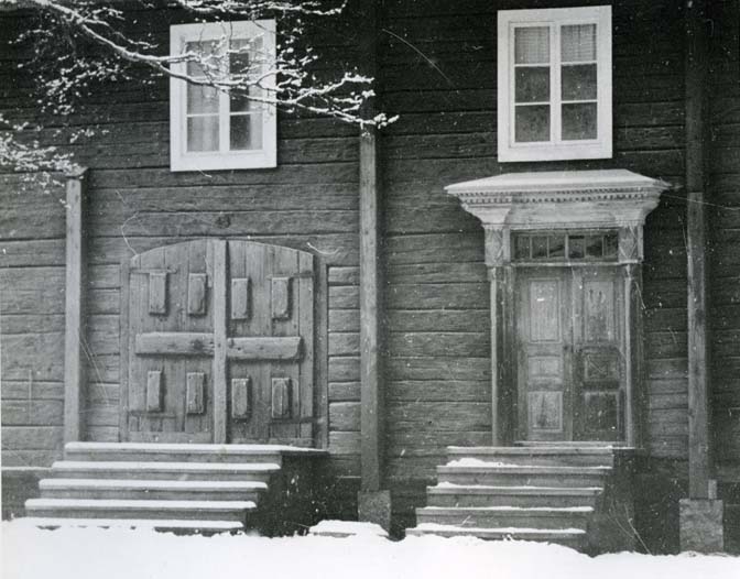 Ett hus vid Hassela hembygdsgård med en dubbelport och en pardörr i en rikt dekorerad dörromfattning.