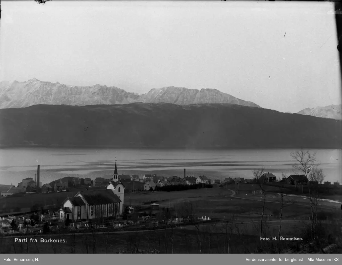 Bilde mot hvitmalt trekirke i Borkenes. Hav og fjell i bakgrunnen.