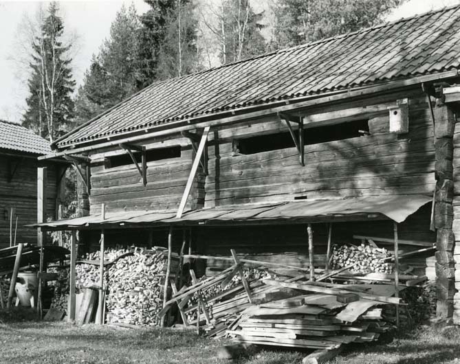 En vedtrave staplad mot en ekonomibyggnad.