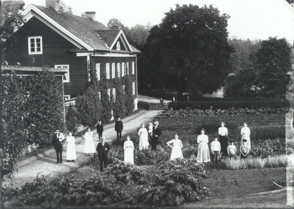 Fotografiet är taget ifrån handelsträdgården som man skymtar på högersidan. Byggnaden till vänster är smedbostaden och i bakgrunden ser man landsvägen och brukssjön.