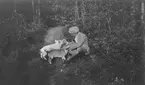 John Bauer sitter vid en skogsstig och har sällskap av en griskulting och en hund.