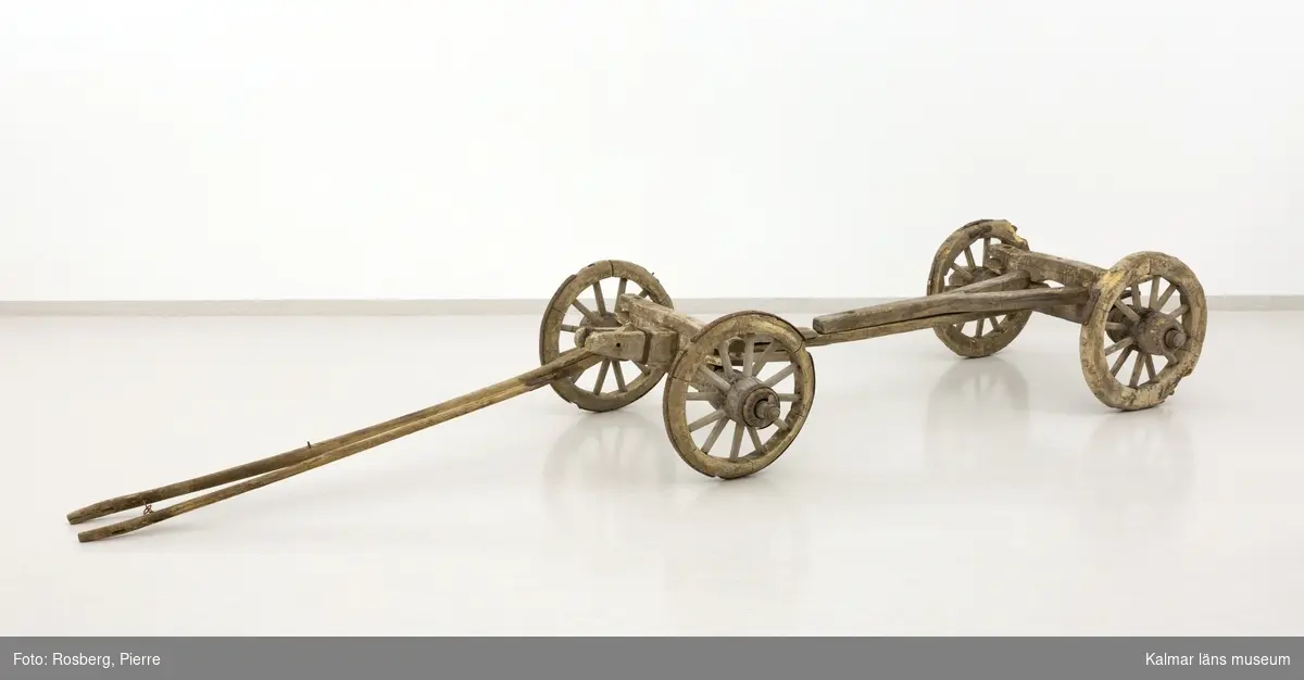 KLM 11833. Bultvagn, hästvagn. Av trä och järn. För hästar. Bultvagn som består av två hjulpar med två bankar, fyra träaxlahjul med järnbeslag, skakel samt dräkt. Det främre hjulparet är mindre än det bakre och har en tillhörande skakel som fästes i en träanordning på dess bank. Dräkten består av en kraftig rektangulär stång av trä med sex stycken borrade hål. Dräkten fästes i en annan träanordning som sitter på motsatt sida av skakeln på det främre hjulparets bank. På det bakre hjulparets bank sitter ett bågformat hål där dräkten sedan förs igenom för att sammankoppla vagnens delar samt justera dess längd. De bakre hjulens nav är dekorerade med zig-zag mönster.