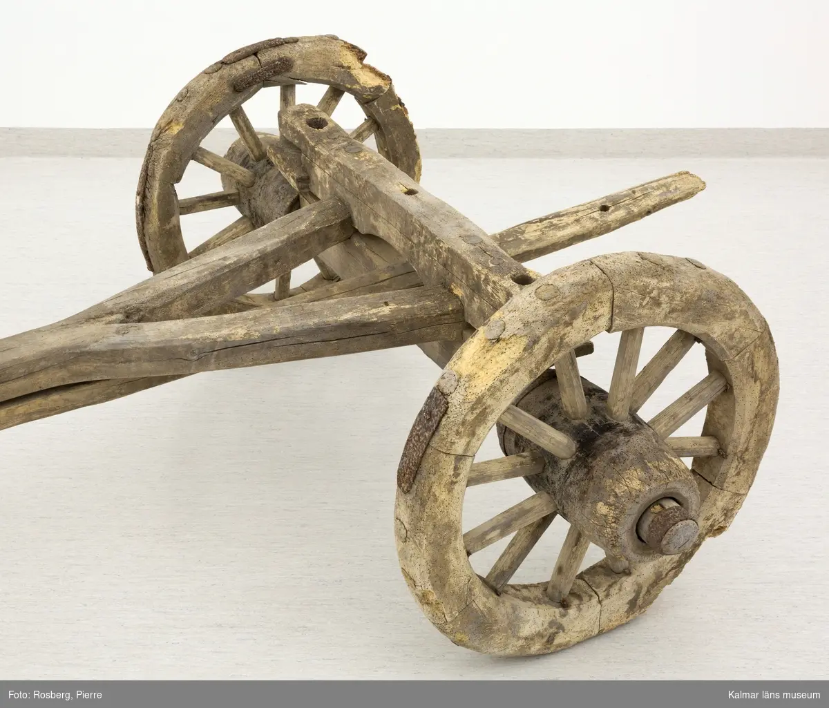 KLM 11833. Bultvagn, hästvagn. Av trä och järn. För hästar. Bultvagn som består av två hjulpar med två bankar, fyra träaxlahjul med järnbeslag, skakel samt dräkt. Det främre hjulparet är mindre än det bakre och har en tillhörande skakel som fästes i en träanordning på dess bank. Dräkten består av en kraftig rektangulär stång av trä med sex stycken borrade hål. Dräkten fästes i en annan träanordning som sitter på motsatt sida av skakeln på det främre hjulparets bank. På det bakre hjulparets bank sitter ett bågformat hål där dräkten sedan förs igenom för att sammankoppla vagnens delar samt justera dess längd. De bakre hjulens nav är dekorerade med zig-zag mönster.